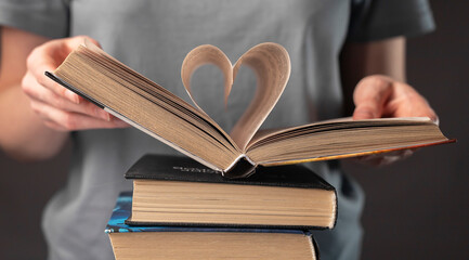 Female hands of book lover holding textbook with heart-shaped pages
