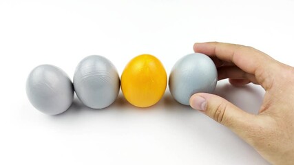 Concept of individuality, exclusivity, better choice. Female hand puts eggs in a row, One yellow egg among gray eggs on white background
