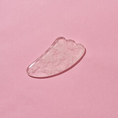 Close up of Rose quartz facial massage Gua Sha scraper isolated over pink background