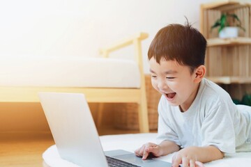 Asian boy using laptop in living room, Cute boy distance learning at home. Online learning