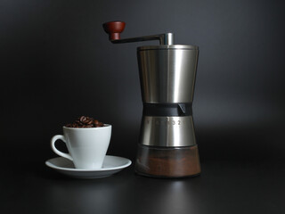 Manual coffee grinder, cup with coffee on a black background.