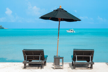 Two chairs and a black umbrella are set on the tropical beach.
