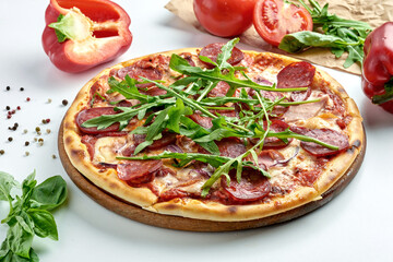 Classic Italian meat pizza with chorizo, salami, ham, cheese, arugula and white sauce on a plate. White background. Italian cuisine, selective focus