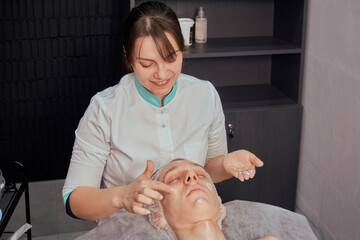 Obraz na płótnie Canvas A female cosmetologist applies a cream to a man's face. Hydration of the skin. Beauty salon.