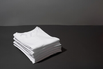 Stack of folded white cotton t shirts isolated over dark gray background