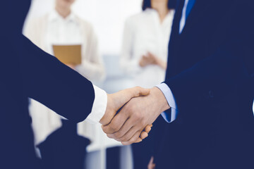 Businessman and woman shaking hands with colleagues at the background. Handshake at meeting in office. Concept of success in business