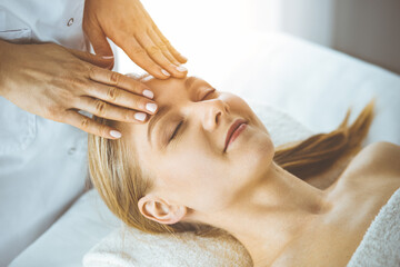 Obraz na płótnie Canvas Happy woman enjoying facial massage with closed eyes in spa salon. Relaxing treatment in medicine and Beauty concept