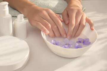 Obraz na płótnie Canvas Elegant, well-groomed female hands with long fingers. Skin care procedure for hands, nails, manicure. Concept of Spa beauty salon. Mocap, plastic containers. Beautiful play of shadows, light on table.