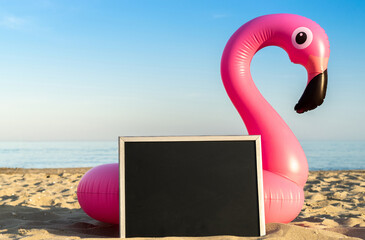 Beach background. Funny pink toy flamingo with blackboard for text on ocean nature beach background...