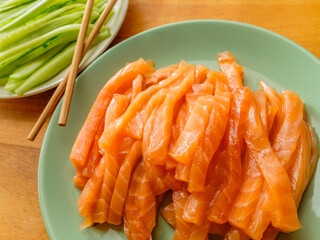 Selective focus on salmon and fresh cucumber slices on plates and bamboo chopsticks. Flat lay. Appetizing vibrant ingredients from Asian cuisine.