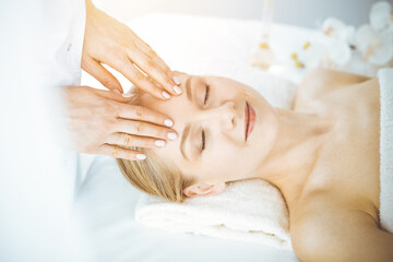 Obraz na płótnie Canvas Beautiful caucasian woman enjoying facial massage with closed eyes in spa salon. Relaxing treatment in medicine and Beauty concept