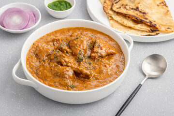 butter chicken, an Indian creamy chicken gravy served in a white bowl with roti or naan