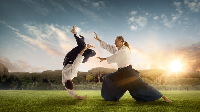 Man and boy, teacher fighting Aikido, training martial arts on meadow in summer evening