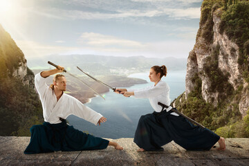 Man and woman, teacher fighting Aikido, training martial arts on meadow in front of lake and...