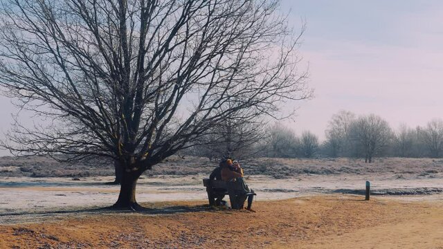 A family sitting on a bench in heath field in Veluwe National Park, Netherlands, wide shot