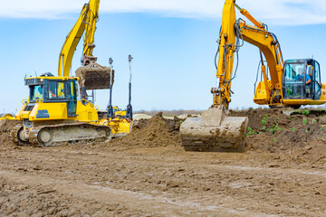 Obraz premium Two excavators and earthmover are leveling ground construction site