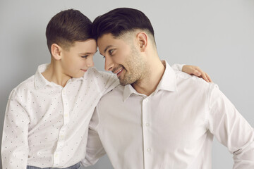 Close up portrait of dad with little son hugging and lovingly looking at each other on gray background. Concept of family, good parents, love, happiness, childhood and fatherhood.