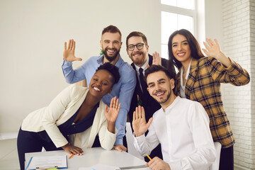 Group portrait of happy multicultural office workers waving hands at camera and smiling. Webcam video chat or teleconference view of team of young mixed race business people saying hello to colleagues - Powered by Adobe