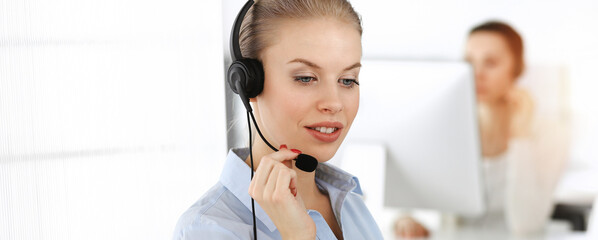 Blond woman working in sunny call center. Group of diverse people working as customer service occupation. Business concept