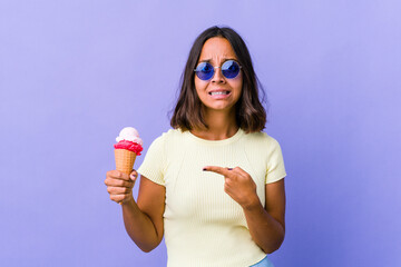 Young mixed race woman eating an ice cream shocked pointing with index fingers to a copy space.