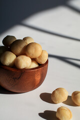 Macadamia nuts in wooden bowl on white table with sunlight and shadow. Macadamia nuts are a source of protein packed with healthy vitamins.