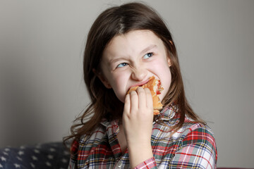 a cute little girl emotionally eating a hamburger, sandwich, cheeseburger or burger and smiling at home
