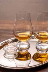 Tasting glasses of single malt scotch whisky served on steel mirror tray with reflection