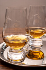 Tasting glasses of single malt scotch whisky served on steel mirror tray with reflection