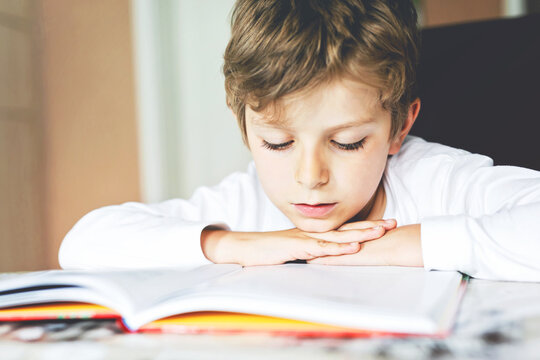 Little blonde school kid boy reading a book at home. Child interested in reading magazine for kids. Leisure for kids, building skills and education concept. Pupil making homework