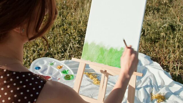 Giovane ragazza dipinge su tela un quadro di natura in campagna