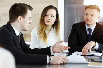 Business people or lawyers discussing questions at meeting in sunny office. Unknown businessman and woman with colleague sitting and working at the glass desk