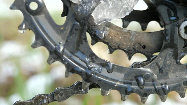 Mountain bike three chainring crankset with oily chain. Snow melting on chainring, wet metal.  Slow motion