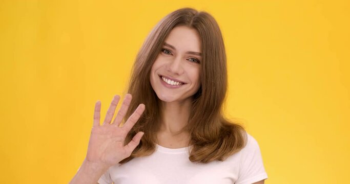 Greeting concept. Cute happy talkative lady waving hand hello and smiling to camera, orange studio background