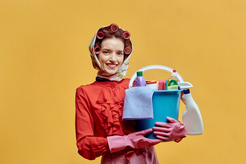 A female cleaner holds a bucket of cleaning tools. He looks at the camera and smiles. Cleaning concept. Pin-up style.