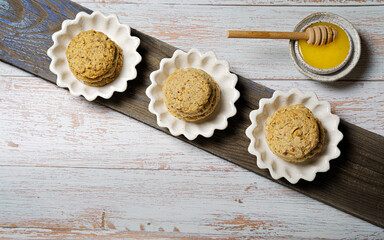 Cookies with almonds-Polvorones on a wooden, textured board and a cup of honey. Top view, copy space. Spanish traditional sweetness.