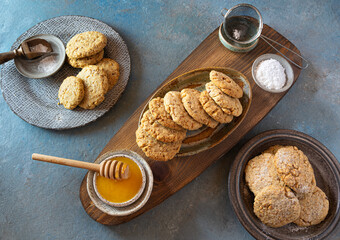 Cookies with almonds-Polvorones on a wooden, textured board and on ceramic plates. A cup of honey and powdered sugar. Top view. Spanish traditional sweetness..