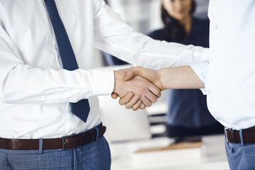 Two businessmen are shaking hands in office, close-up. Happy and excited business woman stands with raising hands at the background. Business people concept