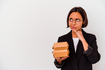 Young business indian woman eating burgers isolated looking sideways with doubtful and skeptical expression.
