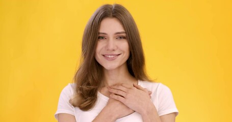 Grateful young woman keeping both palms on chest and smiling to camera, expressing gratitude and good feeling