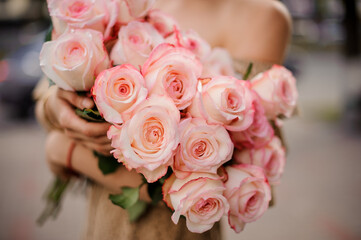 close-up view on beautiful bouquet of fresh light pink roses in hands of woman