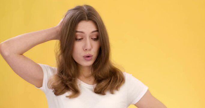 Young emotional lady feeling worried and nervous, scratching her head and shaking head no, orange studio background