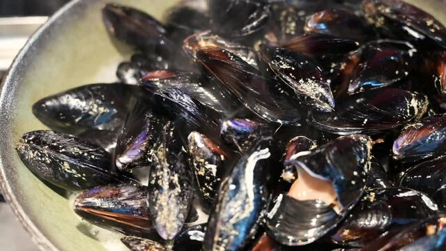 The lid of the saucepan is lifted: it reveals the mussels that are cooking, close up shot. Preparation of a food of the Mediterranean diet.