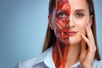 Young woman with half of face with muscles structure under skin. Model for medical training on a...