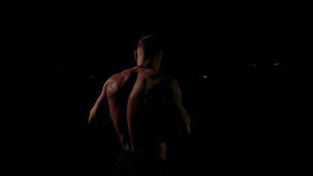 Rear view of a muscular male fighter standing in a dark room against for man silhouettes, unequal confrontation. Stock footage. Four enemies hidden in the shadow, concept of fight with yourself.