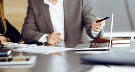 Unknown businessmen and woman sitting, using laptop computer and discussing questions at meeting in modern office, close-up