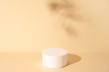 White round podium for cosmetic product against beige background and shadow of leaves. 