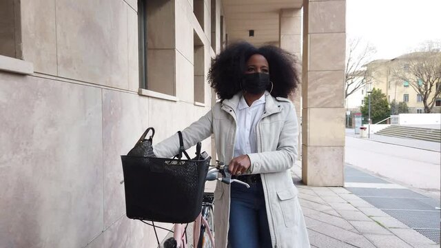 Young commuter woman in city in sustainable way with bike wearing protective face mask against Coronavirus Covid-19 pandemic leads by hand bicycle way home to work - Safety and commuting concept