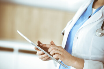 Unknown woman-doctor standing in clinic and using tablet pc, close-up. Data in medicine and healthcare