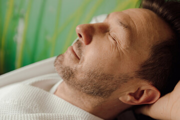 Obraz premium Close up face portrait handsome smiling man enjoying free time in bathrobe with closed eyes. spa relaxation