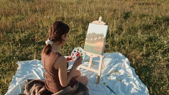 Giovane ragazza dipinge su tela un quadro di natura in campagna